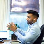 Adult male engaged in a virtual meeting using earphones in an office setting.