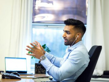 Adult male engaged in a virtual meeting using earphones in an office setting.