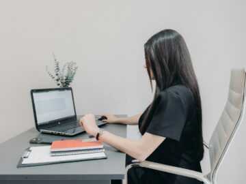 Woman working on laptop at desk with notebooks.