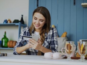 Young woman smiling while using phone and credit card.