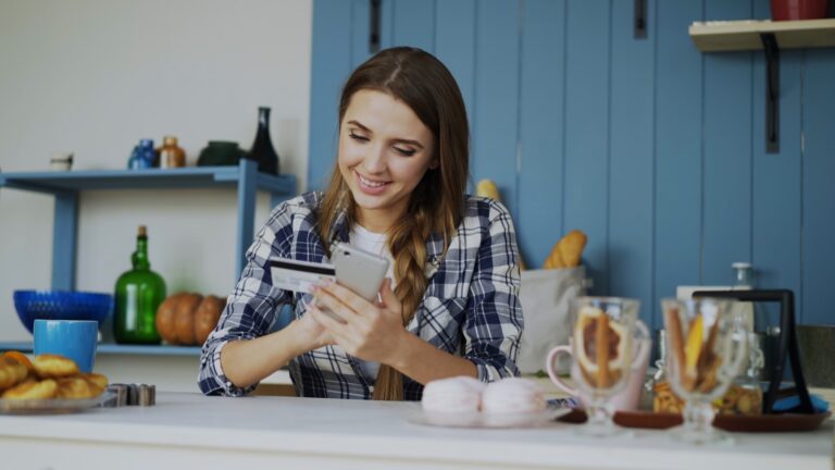 Young woman smiling while using phone and credit card.