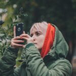 woman wearing green hooded jacket holding iPhone