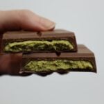 Detailed view of a milk chocolate bar with green filling held in hand against a plain background.