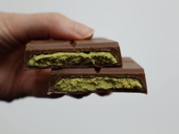 Detailed view of a milk chocolate bar with green filling held in hand against a plain background.