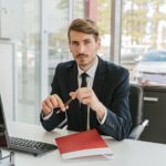 Business professional sitting at a desk with documents in an office environment.