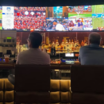 People sitting at a bar watching multiple sports games on large TV screens