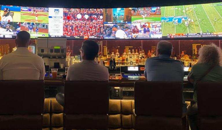 People sitting at a bar watching multiple sports games on large TV screens