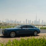 A blue rolls royce parked in front of a city