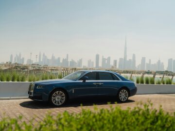 A blue rolls royce parked in front of a city