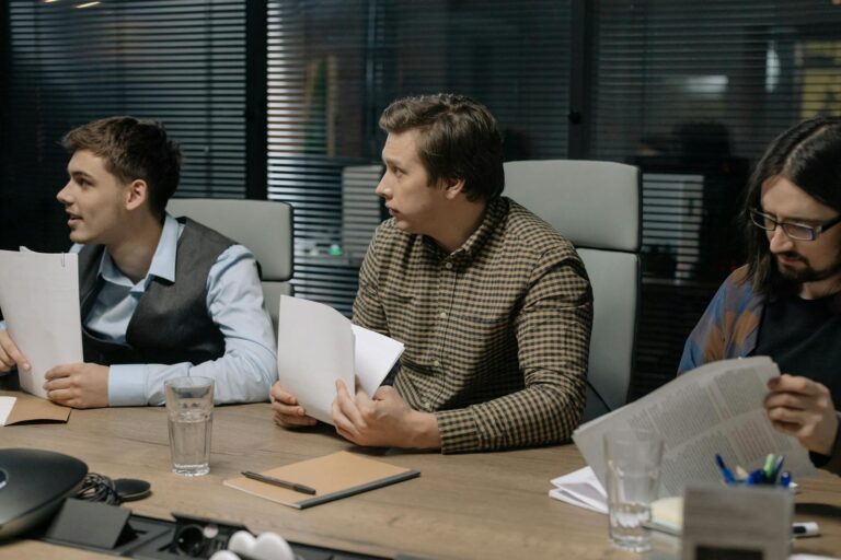 Three male colleagues engage in a business meeting discussing documents around a table.