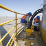 Technicians in safety gear performing maintenance on an offshore wind turbine.