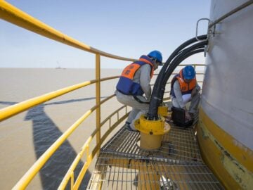 Technicians in safety gear performing maintenance on an offshore wind turbine.