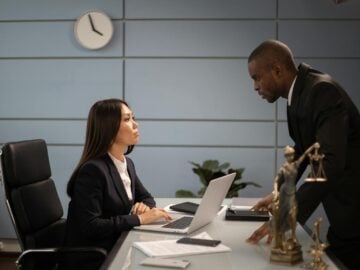 Two colleagues in a formal business setting engaged in a discussion at an office desk.
