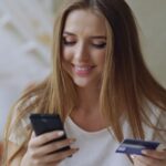 Young woman smiling while holding phone and credit card