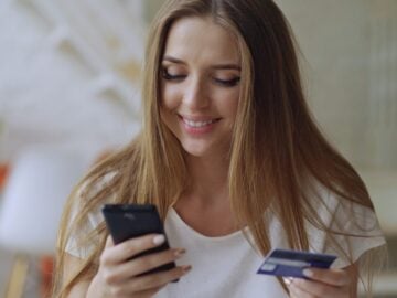 Young woman smiling while holding phone and credit card