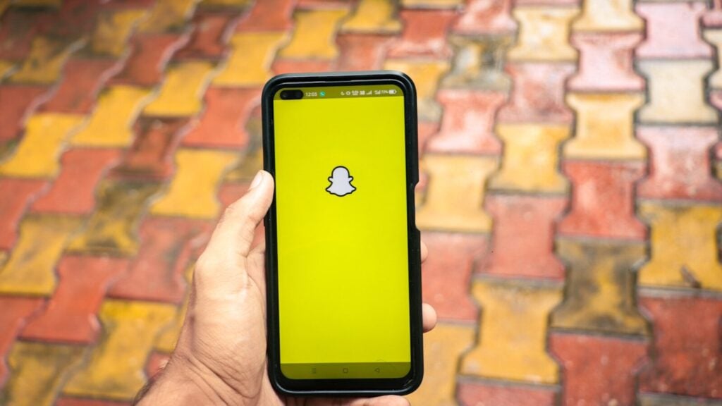 a person holding a cell phone with a snap icon on the screen