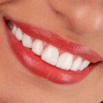 Close-up of a woman's smiling mouth with red lipstick.