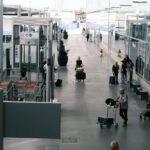 Travelers navigate an airport terminal corridor with luggage carts and suitcases.