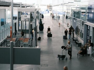 Travelers navigate an airport terminal corridor with luggage carts and suitcases.