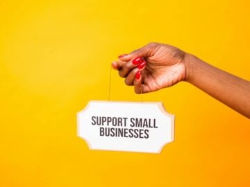 Hand holding a 'Support Small Businesses' sign against a vibrant yellow background, promoting local commerce.