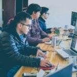 three men facing computer monitors
