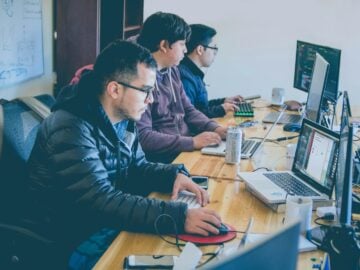 three men facing computer monitors