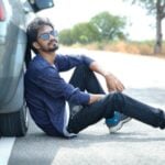 a man sitting on the side of a road next to a car