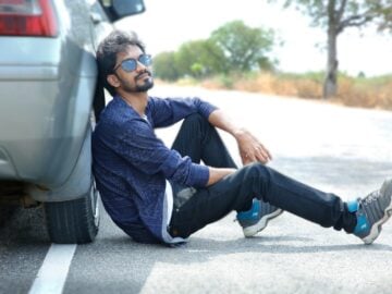 a man sitting on the side of a road next to a car