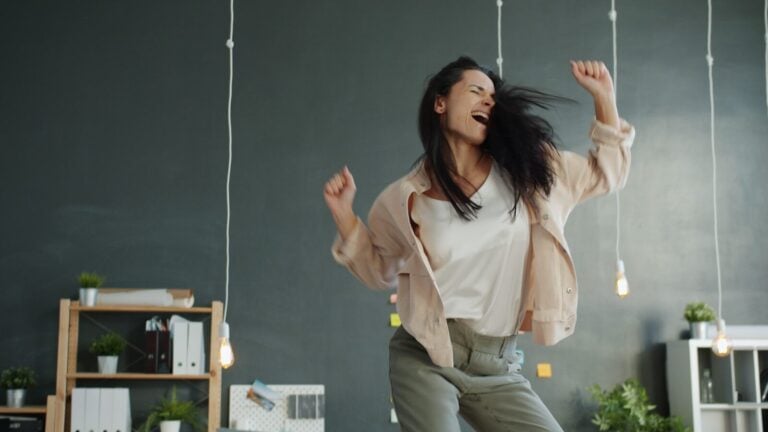 A woman joyfully dancing with arms raised.