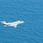 a small white plane flying over a large body of water