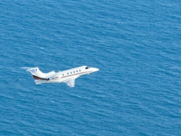 a small white plane flying over a large body of water